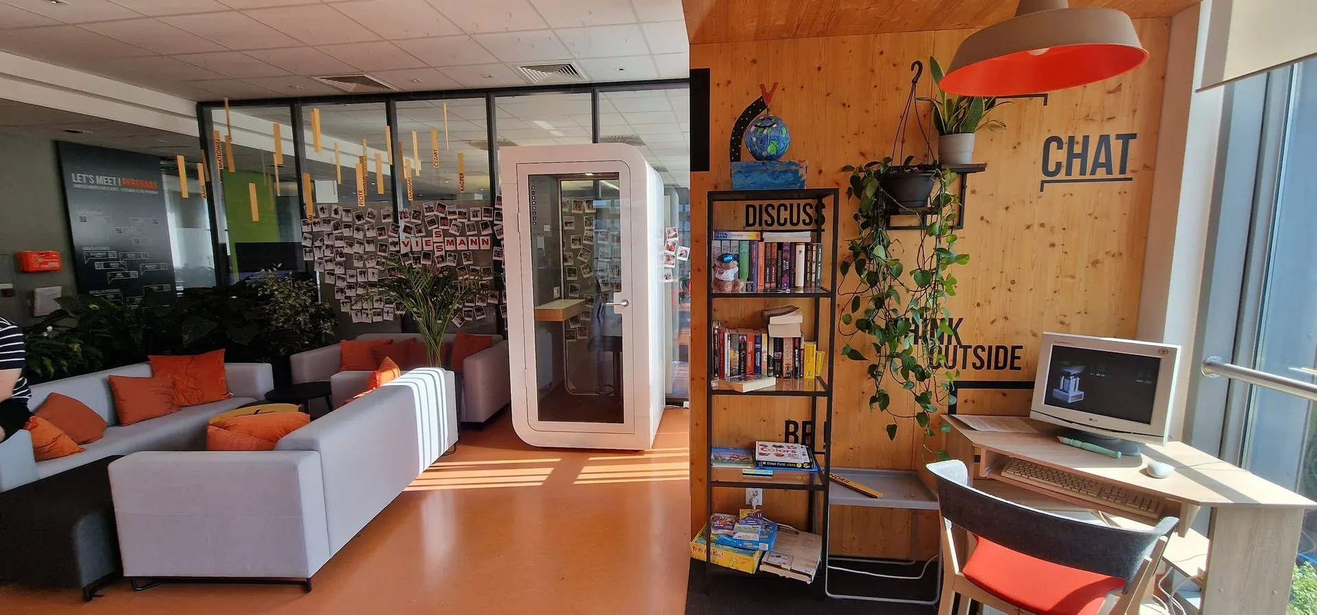 A white single-person Silentbox Solo booth in a bright office lounge with sofas, a bookshelf and plants.